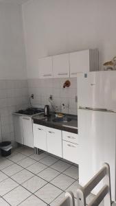 a white kitchen with a sink and a refrigerator at Kitnet in Tramandaí