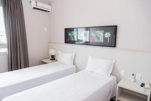 two beds in a hotel room with a tv on the wall at Hotel Eldorado Flat in Contagem