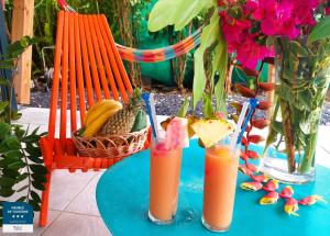 two glasses of orange juice on a table with flowers at Gîtes Les Bienheureux - Piscine, Hamak, Terrasse in Anse-Bertrand