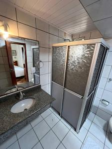 a bathroom with a sink and a shower with a mirror at Acomodare Hotel in Tubarão