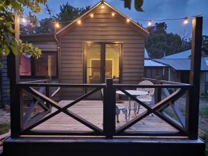 Casa con porche de madera con 2 sillas en Daylesford - Frog Hollow Estate -THE COTTAGE - enjoy a relaxing and romantic night away in our gorgeous little one Bedroom ROMANTIC COTTAGE under the apple tree with water views, en Daylesford