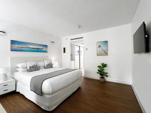 a white bedroom with a large bed and a tv at Palm Cove Beachside Apartments - Sea and Mountain Views in Palm Cove