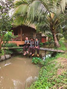 3 Männer sitzen auf einer Brücke vor einem Teich in der Unterkunft MEKONG DANIEL HOMESTAY CAN THO in Cần Thơ