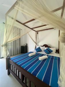 a bedroom with a canopy bed with blue and white pillows at PineApple Surf in Ahangama