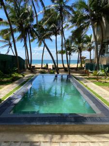 a swimming pool next to a beach with palm trees at Guli Beach Hotel in Hikkaduwa