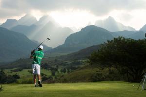 Um homem está a jogar golfe nas montanhas. em Cathedral Peak Hotel em Winterton