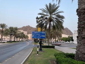 a street sign on the side of a road with palm trees at old muscat in Muscat