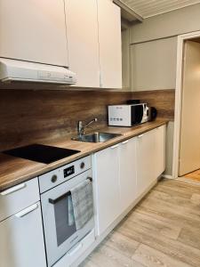 cocina con armarios blancos, fregadero y microondas en FlatsinRoi Apartments, en Rovaniemi