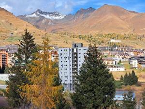 wysoki biały budynek z drzewami przed górami w obiekcie HIGH ALTITUDE Apartment w mieście Passo del Tonale
