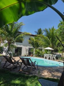 a pool with two chairs and a table and a house at Casa Aroeira Pousada in Ilhéus
