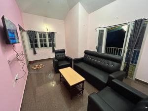 una sala de estar con un sofá de cuero negro y sillas en Dream Ville Homestay en Kodaikānāl