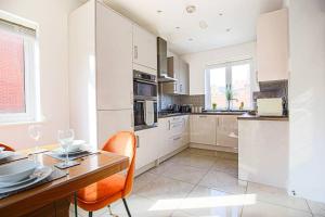 a kitchen with white cabinets and a table with orange chairs at Luxury Detached House with Pool Table, Fast Wi-Fi, Smart TVs and Driveway Parking by Yoko Property in Milton Keynes