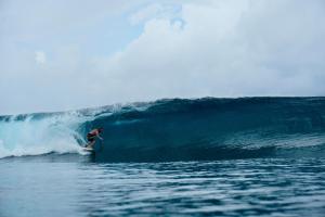 Un uomo che cavalca un'onda su una tavola da surf nell'oceano di Pondok Oma for Solo Traveller a Lasikin