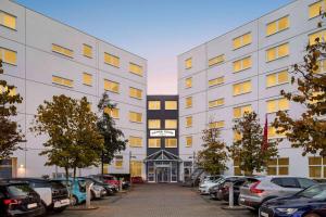 ein großes weißes Gebäude mit Autos auf einem Parkplatz in der Unterkunft Vienna House Easy by Wyndham Neckarsulm in Neckarsulm