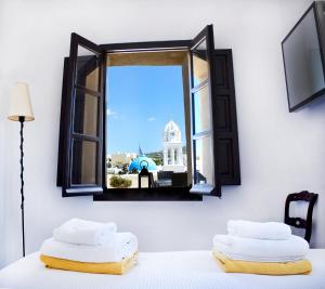 two white towels sitting on a bed looking out a window at Santorini Heritage Villas in Megalochori