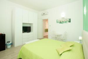 a white bedroom with a green bed and a television at Affittacamere LE RONDINI in Domus de Maria