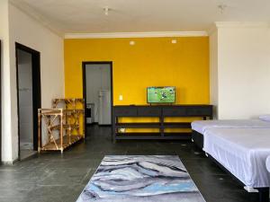 a bedroom with a bed and a tv on a yellow wall at Suítes Temporada Favorita in Peruíbe