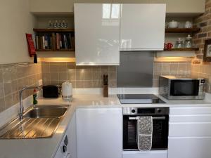 a kitchen with white cabinets and a sink and a microwave at Enchanting 1 Bedroom Home with Kitchen in Saffron Walden