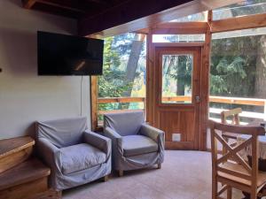 a living room with two chairs and a flat screen tv at BOG Le Pommier - Cabañas con vista al lago y piscina climatizada in Villa La Angostura