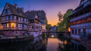 un groupe de bâtiments à côté d'une rivière au coucher du soleil dans l'établissement Studios de la Nuée Bleue, à Strasbourg