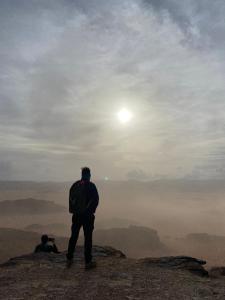 a man standing on top of a mountain looking at the sun at Desert Gate Camp in Wadi Rum