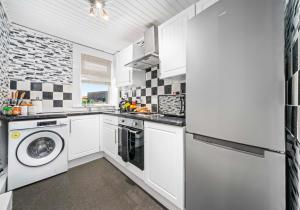 cocina con armarios blancos, lavadora y secadora en Nicol Apartment by Klass Living Airdrie en Airdrie