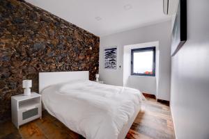 Faja GrandeにあるFontinha Terrace View Houseの白いベッドと石の壁が備わるベッドルーム1室