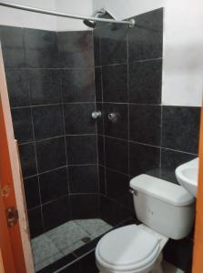 y baño con aseo y ducha con azulejos negros. en Casa Chicama, en Puerto Chicama