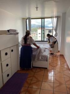 2 Personen machen ein Bett in einem Zimmer mit Fenster in der Unterkunft Hospedaje Alitay in Otavalo