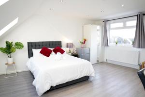 een witte slaapkamer met een groot wit bed met rode kussens bij 32GC Dreams Unlimited - Heathrow Studio Flat w free on-street parking in Staines upon Thames