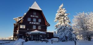 Hotel a restaurace Pomezí في Cínovec: مبنى كبير في الثلج مع شجرة عيد الميلاد