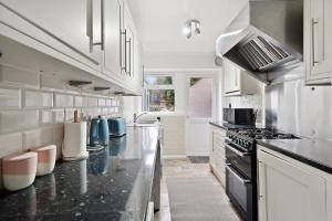 Dunstable 3 bedroom house with Free Parking في دانستابل: مطبخ مع خزائن بيضاء وقمم منضدة سوداء
