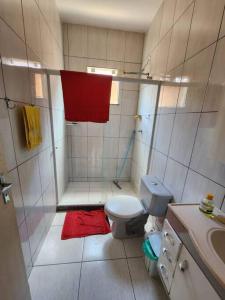 ein Bad mit einer Dusche, einem WC und einem roten Handtuch in der Unterkunft Casa em condomínio em Araruama in Araruama