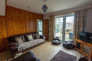 a living room with a leather couch and a television at HILLSIDE COTTAGE - 3 bed property in North Wales opposite Adventure Park Snowdonia in Dolgarrog