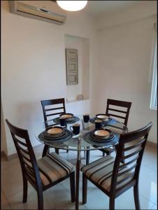 a dining room table with four chairs and a glass table with plates at Los Próceres Apartamento Zona Exclusiva in Tegucigalpa