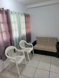 two white chairs and a couch in a room at Casa a 250 metros a pé da praia. Ótima localização in Bertioga