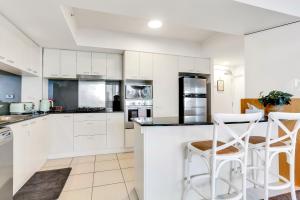 a kitchen with white cabinets and white stools at Glam & Stylish Broadbeach 2BR Apartment in Gold Coast
