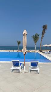 Beach front 2-bedroom villa Privat pool في السيفة: كرسيين ومظلة بجانب مسبح