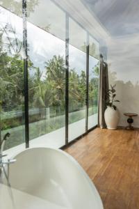 baño con bañera y ventanas grandes en Villa Joyia Ubud, en Ubud