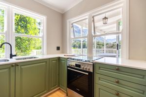 a kitchen with green cabinets and two windows at Exclusive Tree Cottage with hot tub - Power Back-up in Cape Town