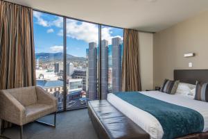 a bedroom with a bed and a chair and a large window at Mantra Collins Hotel in Hobart