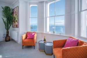 a living room with two chairs and a table and windows at Caldey View - Luxury 2 Bedroom - Panorama - Tenby in Tenby
