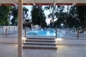 uma piscina com cadeiras brancas e uma mesa em Giardini Sausari Residence em Punta Prosciutto