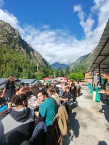 eine Gruppe von Menschen, die an Tischen mit Bergen im Hintergrund sitzen in der Unterkunft NEW SAMY CAFE AND HOMESTAY in Kasol