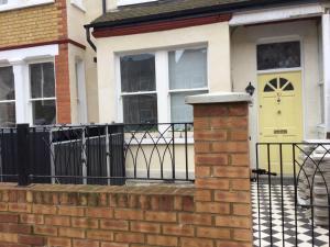 a house with a yellow door and a fence at TDM Bachelot Lettings Ltd in London