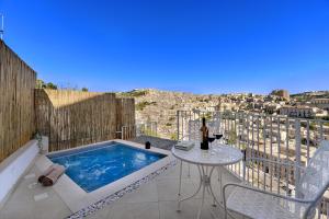 Un balcón con una piscina profunda y una mesa con una copa de vino. en Itria Modica, en Módica