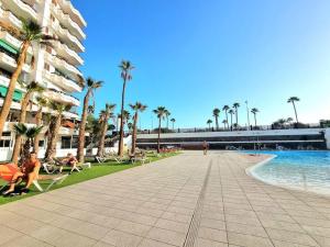 a walkway next to a beach with palm trees and a building at Un pisito en Maspalomas in Maspalomas
