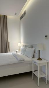 a white bedroom with a bed and a table with a lamp at The Ocean Villa in Fujairah