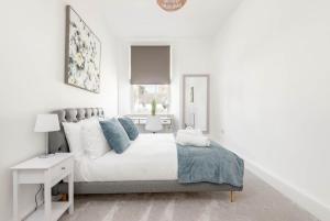 a white bedroom with a large white bed with blue pillows at Skye Sands - The Eden Residence in St. Andrews +2 photos
