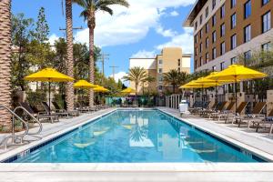 einen Pool mit Stühlen und Sonnenschirmen in einem Hotel in der Unterkunft Home2 Suites By Hilton Anaheim Resort in Anaheim